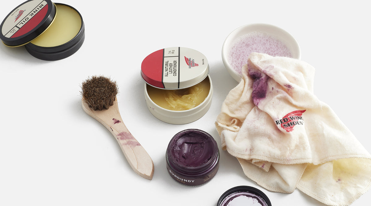 Red Wing shoe care products, brush and cleaning cloth arranged on a white background.